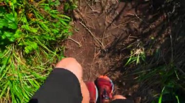 Yeşil çimlerle yürüyen bir adamın yakın çekimi. Şarjör. Spor ayakkabılı bir adam güneşli yaz gününde dağ yolunda yürür. Spor ayakkabıları dar yolda yeşil çimlerle yürür. 