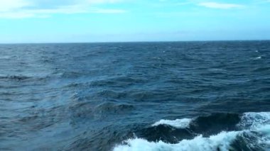 Dalgalı mavi denizin güzel manzarası. Şarjör. Mavi denizdeki yüzen gemi dalgalarından köpük. Mavi denizde, arkadaki dalgalarla mavi gökyüzü. 