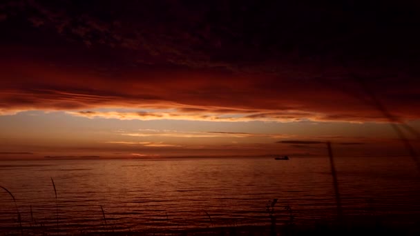 童话般令人叹为观止的落日 飘荡在水面上 飘荡着一条漂浮的小船 深红色和橙色的天空 厚重的云彩在水面之上 — 图库视频影像