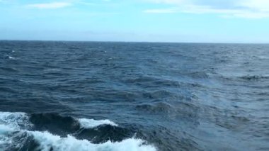 Dalgalı mavi denizin güzel manzarası. Şarjör. Mavi denizdeki yüzen gemi dalgalarından köpük. Mavi denizde, arkadaki dalgalarla mavi gökyüzü. 