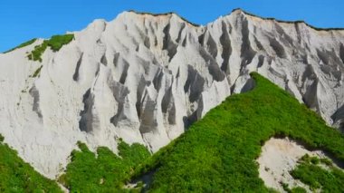 Yeşil çimenli muhteşem beyaz dağlar. Şarjör. Güneşli yaz gününde parlak yeşillikle kayalık beyaz dağda güzel desenler. Yaz günü adaya volkanik kökenli beyaz kayalar. 