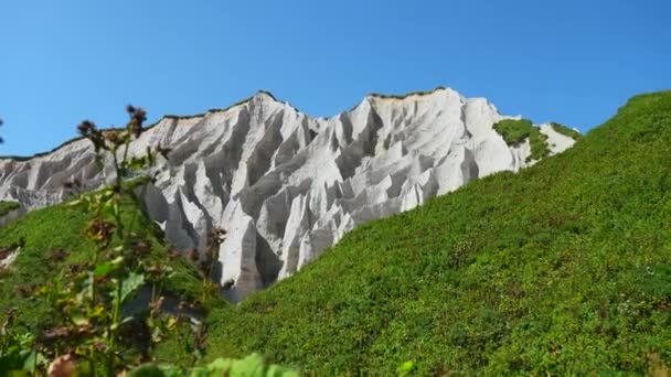 緑色の草で素晴らしい白い山 クリップ 晴れた夏の日の明るい緑の岩の白い山の美しいパターン 夏の日に島で発生する火山起源の白い岩 — ストック動画