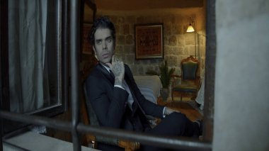 Kameraya poz veren bir adam. Aksiyon. Kolunda dövmesi olan zarif bir adam penceresinin kenarında deri sandalyelerle güzel bir stüdyoda çekilmiş bir takım elbiseyle oturuyor. Yüksek kalite 4k