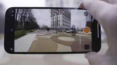 Telefonun video çektiği ekrana yakın çekim. Başla. Adam telefonu tutuyor ve oyun parkı ve çok katlı binanın videosunu çekiyor..