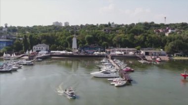 Akşamları limanda lüks yatlar. Deniz manzarasında yelken açmak. Günbatımında hava manzarasında yelkenli ve yat kullanmak. Gün batımında liman, arka planda güzel bir gökyüzü ve orman 4K