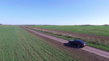 Araba, hava sahasından geçerek yola çıkıyor. Görüntü. Araba, tarlalar ve ormanlar boyunca güneşli yolda gidiyor. Yolun kenarından görüntüle HD