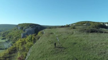 Mavi gökyüzünün altında tepenin üstüne yürüyen adam. Üstten harika görünüm