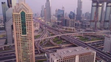 Modern gökdelenleri ve Dubai şehir merkezindeki lüks gece otobanlarını seyret. Kule çatısından üst hava manzarası. Yol kavşağı trafiği. Dubai şehir merkezinin güzel gündüz manzarası 4K