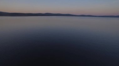 Ufukta dağlar olan bulutlu bir günde tepeden deniz manzarası. Güzel gün batımı ve akşam gökyüzü, deniz manzaralı dağ ve bulutlar 4K