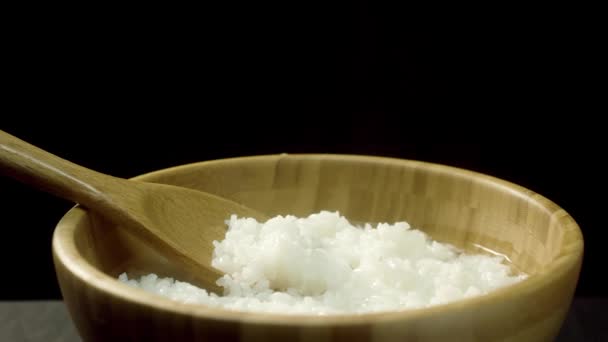 煮熟的 美味的 热的米饭与蒸汽在木锅和大勺子 隔离在黑色的背景 以蒸饭 健康饮食理念为深菜而靠近 — 图库视频影像