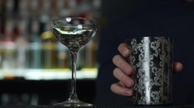 Küçük boş kokteyl bardağına buz koyan bir barmene yaklaş. Medya. Arka planda bulanık alkol şişeleriyle içki yapmanın ayrıntıları.