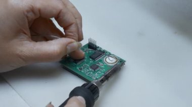 Servis merkezinde bilgisayar parçaları tamir eden genç bir adam. Yaratıcı. Çipi lehimlemeye yakın tut.