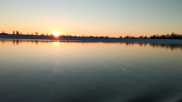夜明けに冬の湖の表面にセーリング クリップ 地平線に夜明けの太陽を反射した美しい水の広がり 明るい太陽が昇る冬の海岸の美しい水 — ストック動画