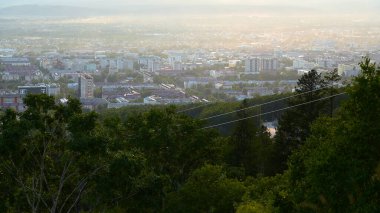 Yazın şehir manzaralı güzel bir teleferik manzarası. Şarjör. Yamaçta yeşil orman, kasabanın sınırında hareket halindeki kablolu yollar. Vadide güzel bir şehir, güneşli bir yaz gününde teleferiği var..