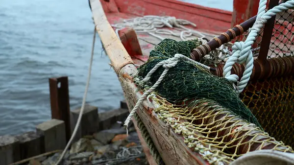 Close-up of fishing boat on wooden pier. Clip. Fishing nets on wooden boat standing on sea pier. Beautiful details of sea fishing boat on cloudy day.