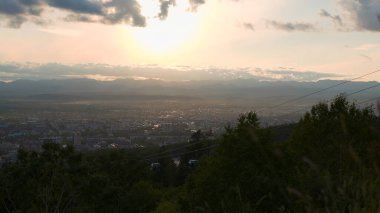 Teleferiği olan güzel bir şehir manzarası. Şarjör. Dağ ufkunun arka planındaki vadide güneşli şehir manzarası. Güneşli bulutlu hava vadide kasaba ve teleferikle birlikte..