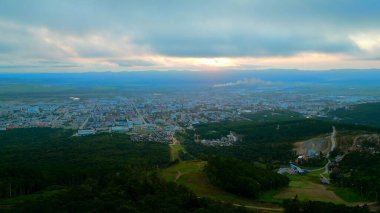 Yeşil dağlardan turist kasabasına doğru uçan hava aracı. Şarjör. Tepenin yamacındaki yeşil ağaçlar ve bulutlu gökyüzü