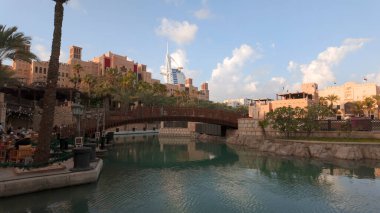 Dubai - BAE, 3 Ocak 2024: Turkuaz suyla Dubai kanalı manzarası. Başla. Restorandaki turistler ve arka plandaki villalar.