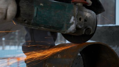 Adam dairesel testereyle metal boru kesiyor. Şarjör. Sıcak metalden kıvılcımlar saçılıyor. Çelik üzerinde sıkı çalışan adam.