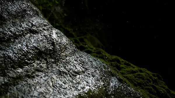 Mossy mountain slope with drops of water falling down. Creative. Enter into a dark large cave