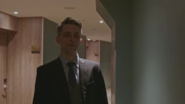 Otel koridorundaki odalarda yürüyen bir güvenlik görevlisi. Borsa klipsi. Karanlık bir binada takım elbiseli genç bir adam. 