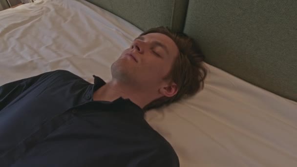 年轻人穿着衣服躺在床上 失去知觉或精疲力竭 库存夹 白人男性躺在床上 眼睛闭着 — 图库视频影像