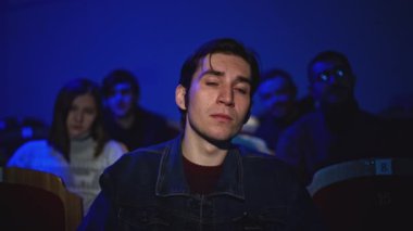 Genç adam tiyatro gösterisi izliyor. Medya. Adam tiyatro performansını yerinde seyrediyor. Seyirci, tiyatro performansındaki spot ışıklarıyla aydınlatıldı.