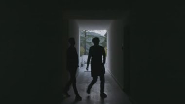 İki erkek siluet karanlık, uzun otel koridorunda yürüyor. Borsa klipsi. Siyah salonda erkek figürleri