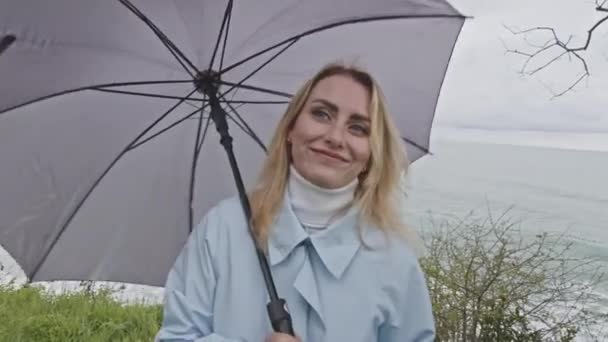 年轻的微笑的女人 满眼充满爱心地旋转着灰色的雨伞 库存夹 穿着外套的女孩在海滨与人交谈 — 图库视频影像