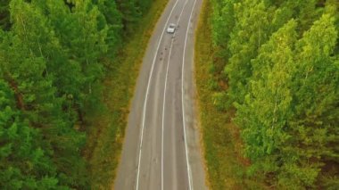 Gürcistan ormanlarında güneşli bir yaz günü üstü açık arabaların kır yolu boyunca sürüşü. Görüntü. Sinematik İHA, tek arabayla güzel boş bir yolun görüntüsünü yakalıyor.