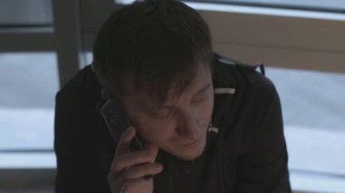 Adam heyecanla telefonla arıyor. Hisse. Adamın arayıp telefonla konuştuğu yakın plan. Adam pencerelerin arka planında telefon görüşmesi yapıyor.