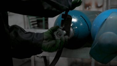 Gaz tüpü kapakçığı çeviren eldivenli işçilere yaklaş. Şarjör. Fabrikanın endüstriyel arka planı