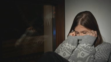 Evin penceresinde depresyon geçiren genç bir kadın. Medya. Pencerede oturan süveterli genç bayan. Depresyondaki bekar bir kadın geceleri evin penceresinde uyuyakalır..