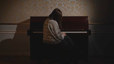 Genç bir kadın ne yazık ki piyanonun başında oturuyor. Medya. Piyanonun başında oturan kadının arka görüntüsü. Kadın üzgün bir şekilde eski piyanonun başına oturur ve hiç çalmaz..