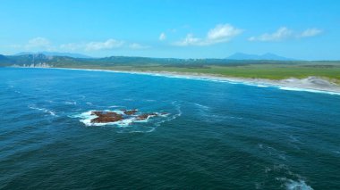 Güzel İzlanda doğa kıyısı yukarıdan. Şarjör. Mavi su yüzeyinde taş oluşumları ve uzaktaki çayırlar.