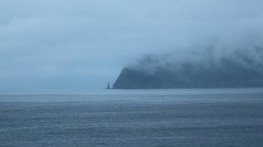 Düşük bulutlu kayaların inanılmaz denizi. Şarjör. Bulutlu bir havada, koyu kayalıklı mavi deniz. Sahildeki kayalıkları kaplayan dramatik alçak bulutlu deniz manzarası.