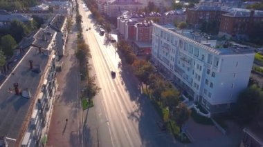 Günbatımında yeşil ağaçlar üzerinde uçmak, modern şehir manzarası. Şarjör. Evleri ve hareket eden arabaları olan şehir caddesi.