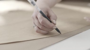 Siyah kalemle kahverengi kağıda çizim yapan bir elin yakın çekimi yaratıcı bir tasarım sürecini gösteriyor..