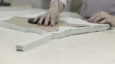 Elbise atölyesinde testereyle kumaş kesen ellerin yakın çekimi, incelik ve ustalığı gösteriyor..