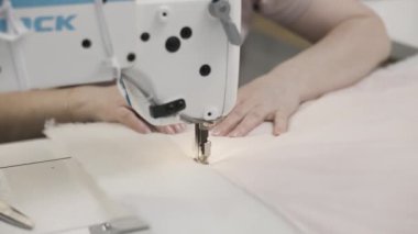 Dikiş makinesinden kumaşa rehberlik eden, titiz dikişleri gösteren ellerin detaylı yakın çekimi..