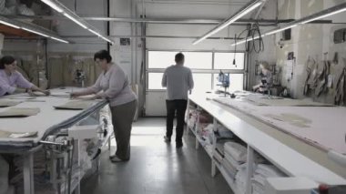 Tasarım stüdyosundaki işçiler kumaş kesimine, işçiliğe ve detaylara özen gösteriyorlar.