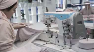 Tekstil fabrikasında endüstriyel dikiş makinesi kullanan bir terzi. Üretim için kumaş kırıştırıyor.