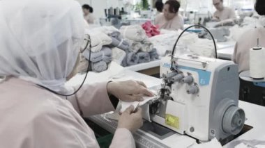 Fabrika işçileri üretim ve otomasyonu vurgulayarak endüstriyel bir ortamda elbise yapmak için dikiş makineleri kullanırlar.