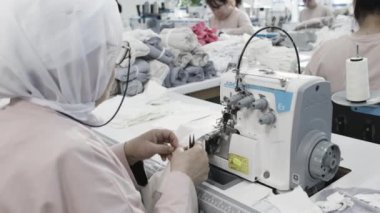 Tekstil fabrikası işçilerinin yakın çekimi endüstriyel makinelerle dikiş dikmek, toplu giysi üretimi üzerinde çalışmak..