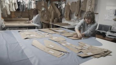 İşlek bir atölyede kumaş ve desenleri kesip düzenleyen terziler, ayrıntılı moda tasarımları yaratıyorlar..
