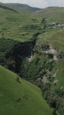 Arka planda bulutlar olan büyük, güzel bir kayanın havadan görünüşü. Başla. Yeşil yamaçlarla dağların üzerinde uçuyor