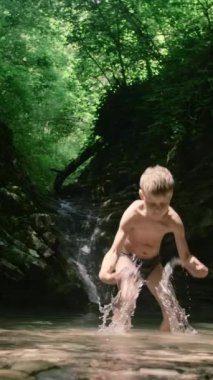 Yolculuktaki bir çocuk. Yaratıcı. Suda oynayan külot giymiş küçük bir çocuk ve uçurumdan gelen büyük kayalar arkadan görülebiliyor. Yüksek kalite 4k görüntü