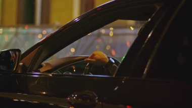 Mans direksiyonun başına geçti. Şarjör. Direksiyonda erkek eli olan bir arabanın penceresinden bak. Gece şehrinde zengin bir adam araba kullanıyor.. 