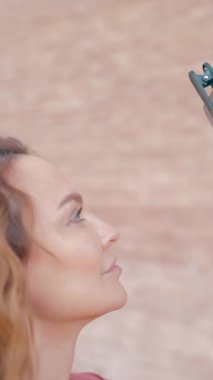 Güzel genç bir kadın video çekiyor. Başla. Uzun saçlı güzel bir kadın iPhone 13 'te harika aksesuarları olan videolar çekiyor. Yüksek kalite 4k görüntü