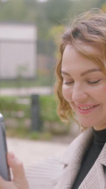 Güzel bir kadın sokakta videoyla iletişim kurar. Başla. Şık bir kadın video bağlantısıyla konuşuyor ve gülümsüyor. Telefondaki videolu mutlu kadın..
